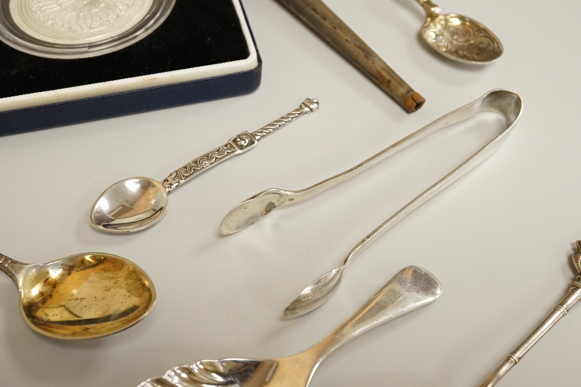 Assorted small silver including a mounted ribbed glass match strike, height 40mm, a small Scottish sterling spoon by Hamish Dawson Bowman, 76mm, a pair of George IV silver sugar tongs, commemorative spoons, an early 20th
